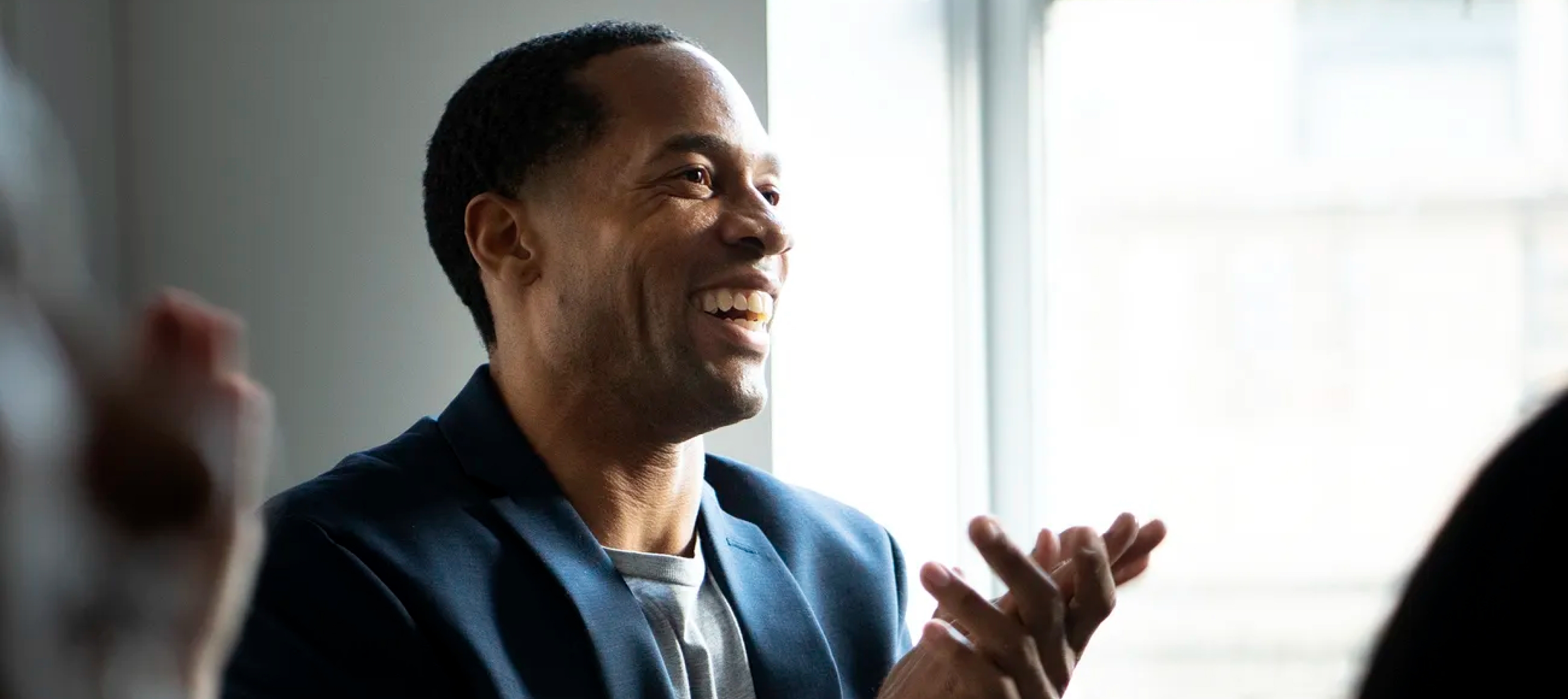 <p>Image of a middle aged man dressed in a blazer, clapping his hands while smiling.</p>
