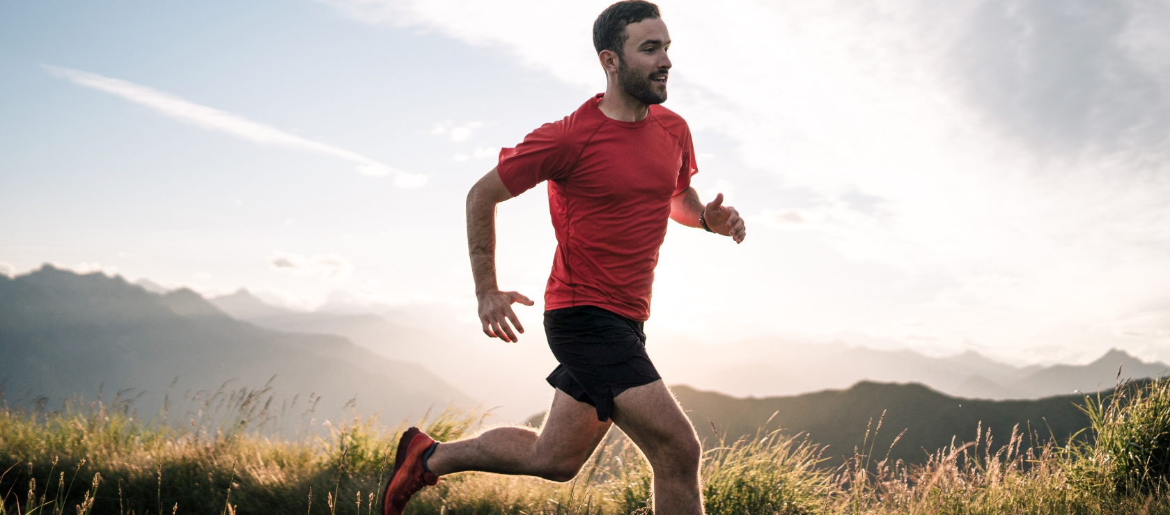 <p>Middle aged man running in a field of grass, surrounded by mountains.</p>
